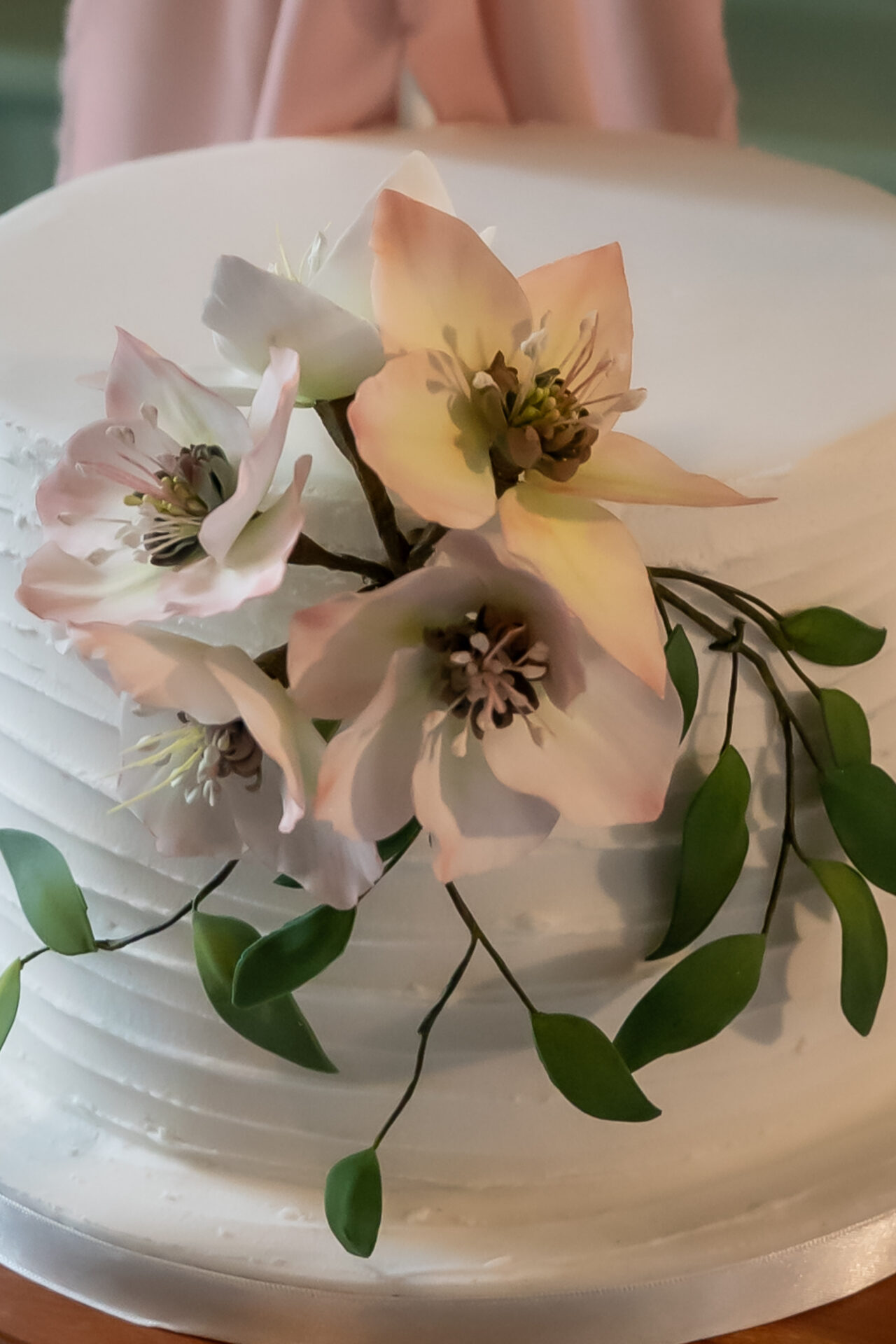 Picture shows the bottom tier of a white wedding cake with a ruffled finish, and three handmade sugar hellebores with ruscus leaves. Photo taken by Emily-Jane Photography at The Pepper Mill in Devizes