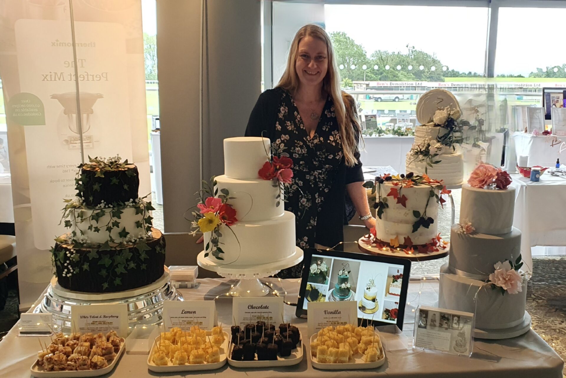 Picture of Louise standing behind her display cakes at a wedding fair at Bath Racecourse