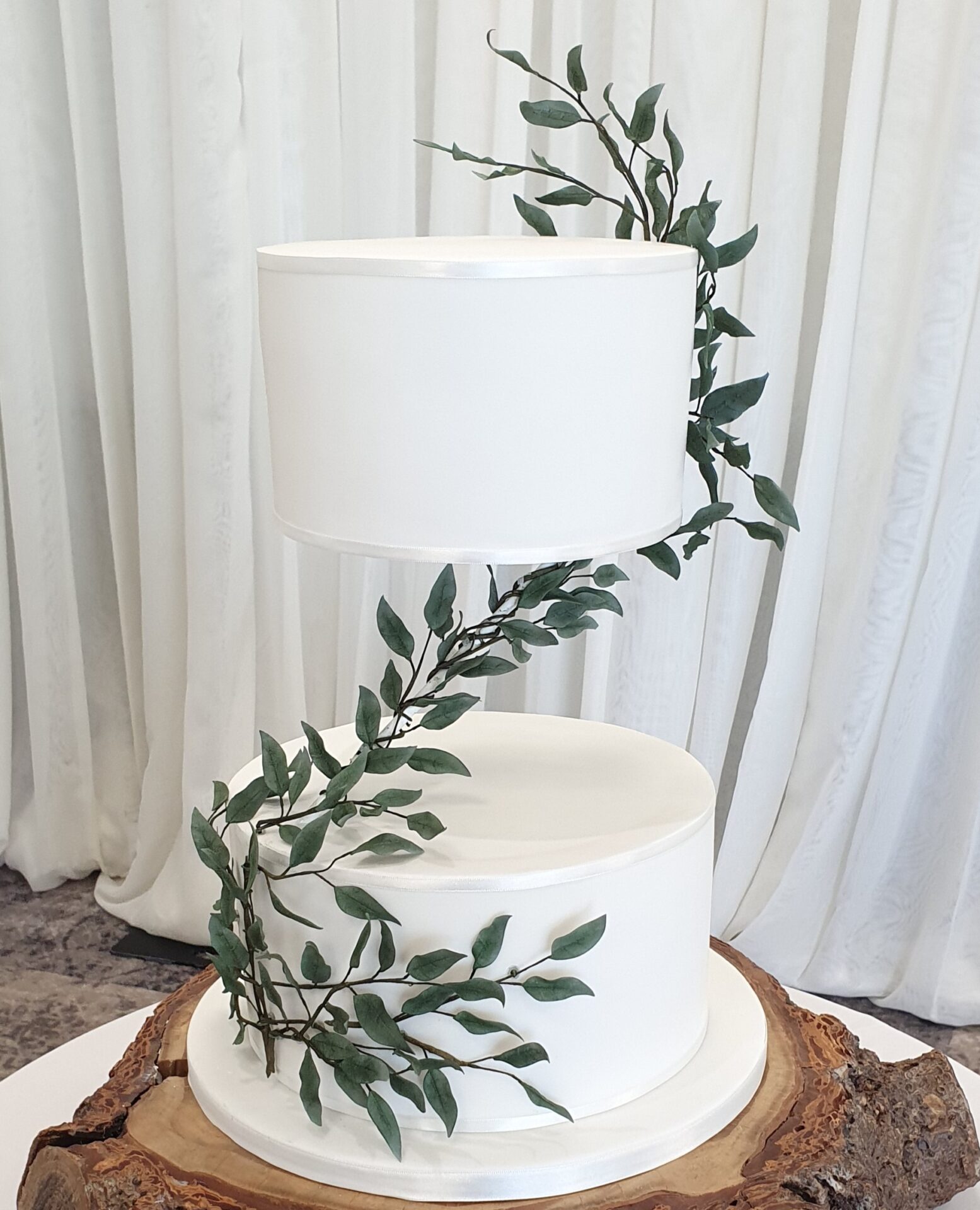 Two tier white wedding cake with floating top tier. Featuring handmade green sugar ruscus leaves snaking from bottom left , up across the Z separator to top right.